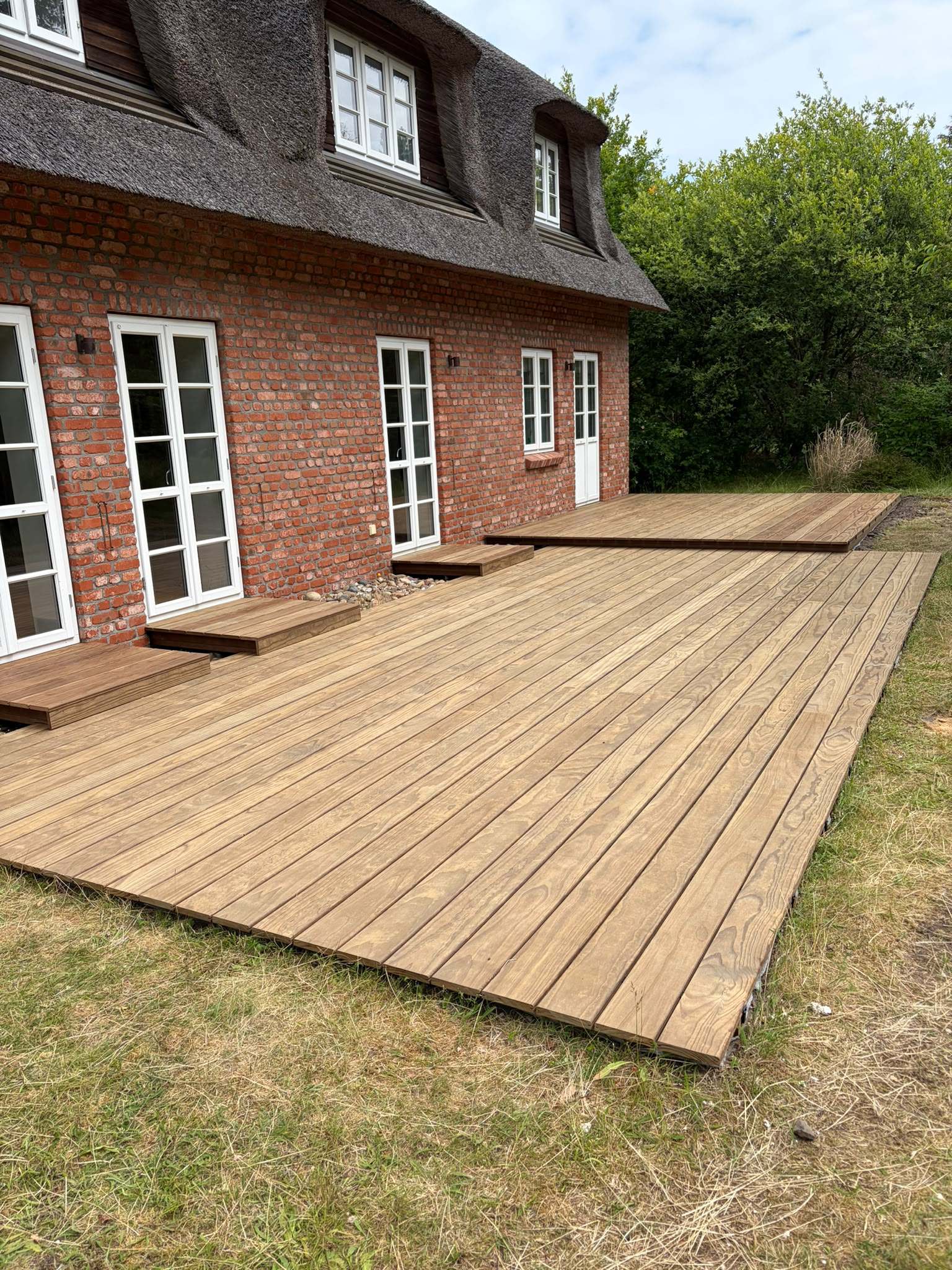 Neue Holzterrasse an einem Reetdachhaus
